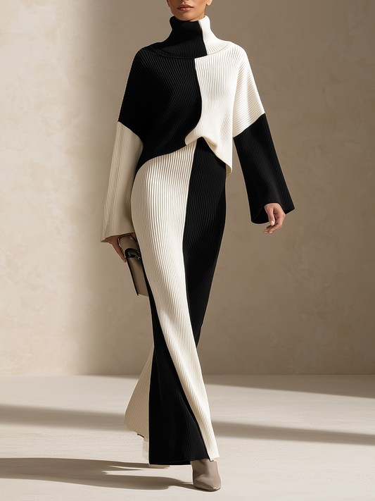 A model wears a long-sleeved, high-neck ribbed knit dress with a bold black and off-white color-blocked design, styled with neutral beige ankle boots against a textured beige studio backdrop.